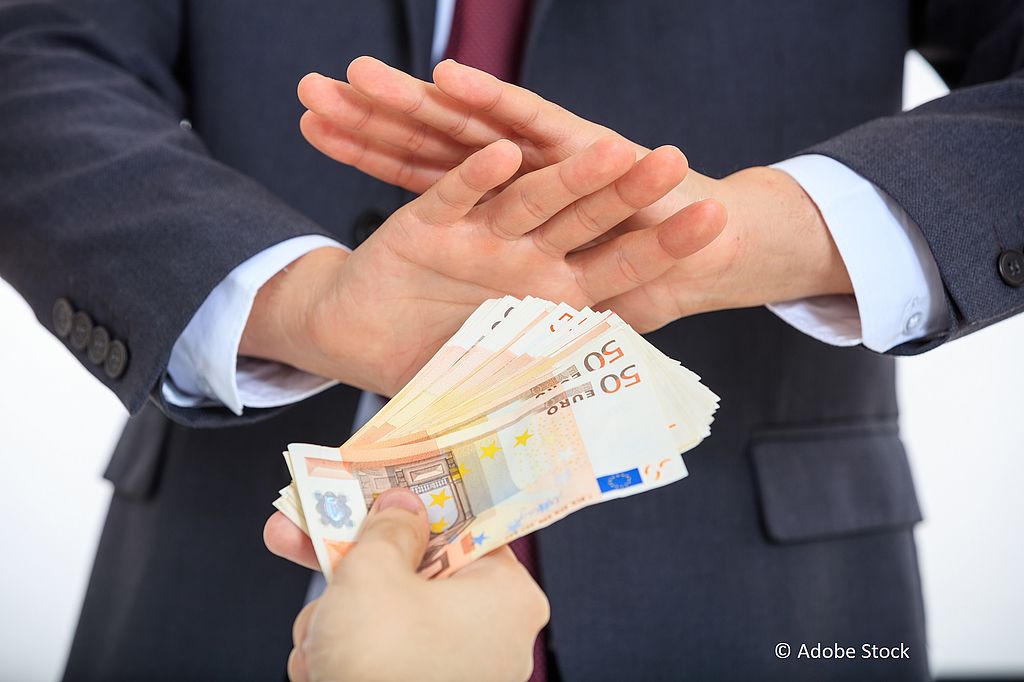 Eine Person mit Anzug verwehrt mit den Händen die Annahme von angebotenen Geldscheinen.