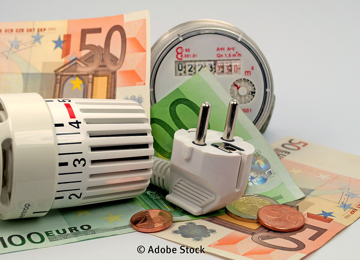 Energieverbrauch Adobe Stock Auf dem Bild sind ein Thermostat, ein Stecker und ein Stromzähler neben verschiedenen Geldscheinen abgebildet.