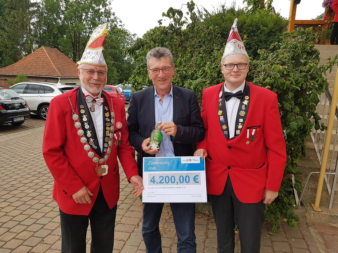 Minister Dieter Lauinger überreicht zwei Mitgliedern des Günzerodaer Karnevalsvereins einen Lottomittelscheck