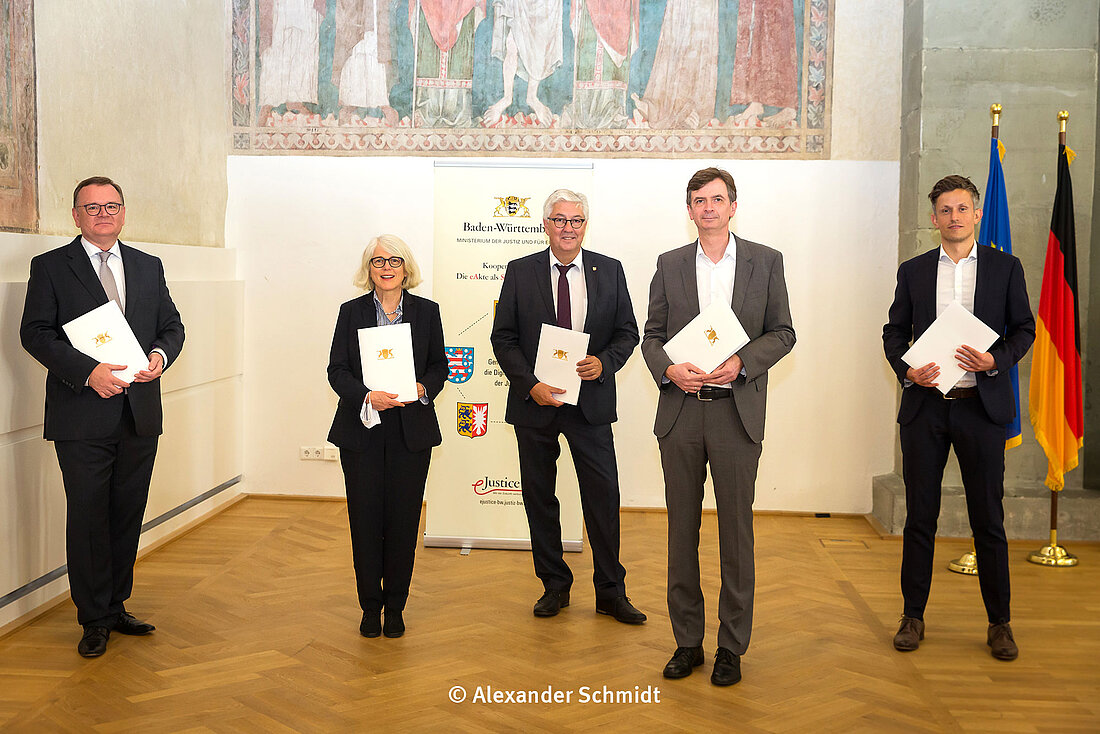 Ministerialdirektor Elmar Steinbacher, Staatssekretärin Dr. Margaretha Sudhof, Staatssekretär Wilfried Hoops, Staatssekretär Sebastian von Ammon und Staatssekretär Mathias Weilandt (von links) stehen nach Unterzeichnung der Kooperationsvereinbarung vor einem Rollup und halten eine Mappe mit der Vereinbarung in der Hand.  (Foto: Alexander Schmidt)