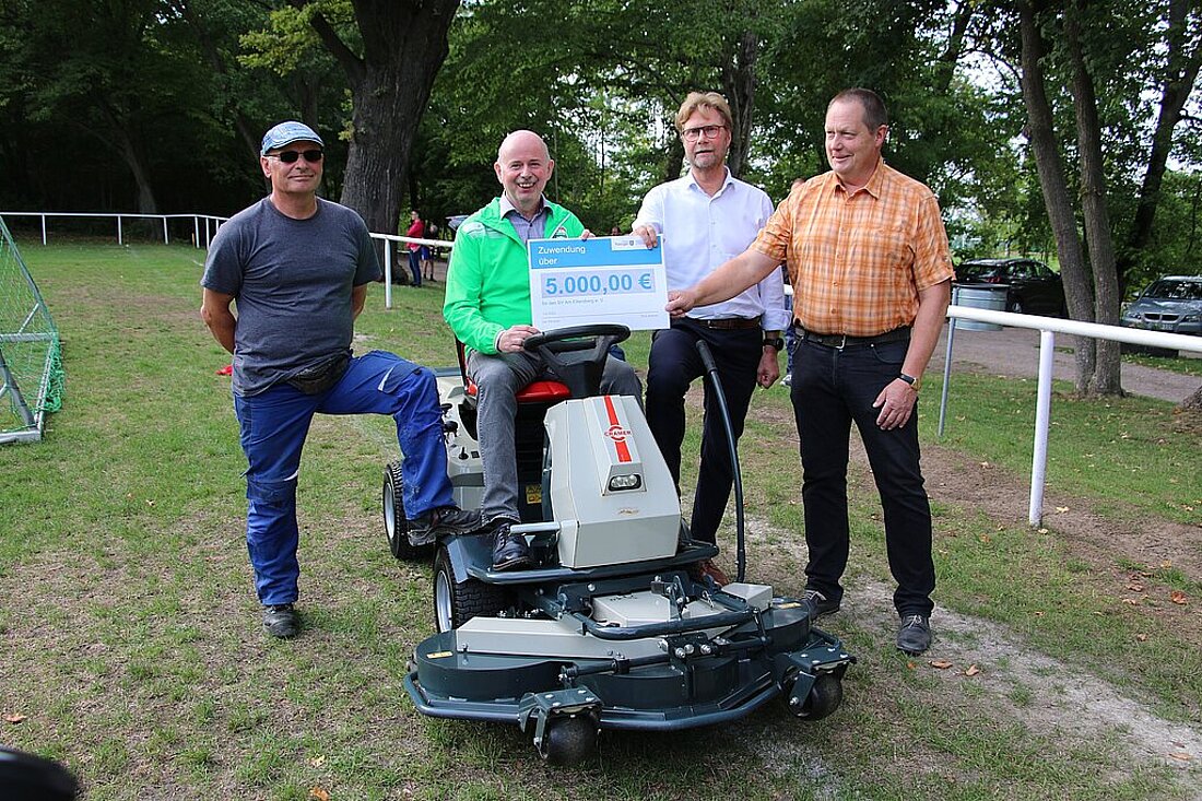 Minister Dirk Adams und Mitglieder des Vereins Ettersburg e.V. auf dem Vereinsgelände mit dem Rasentraktor und dem Lottomittelscheck.