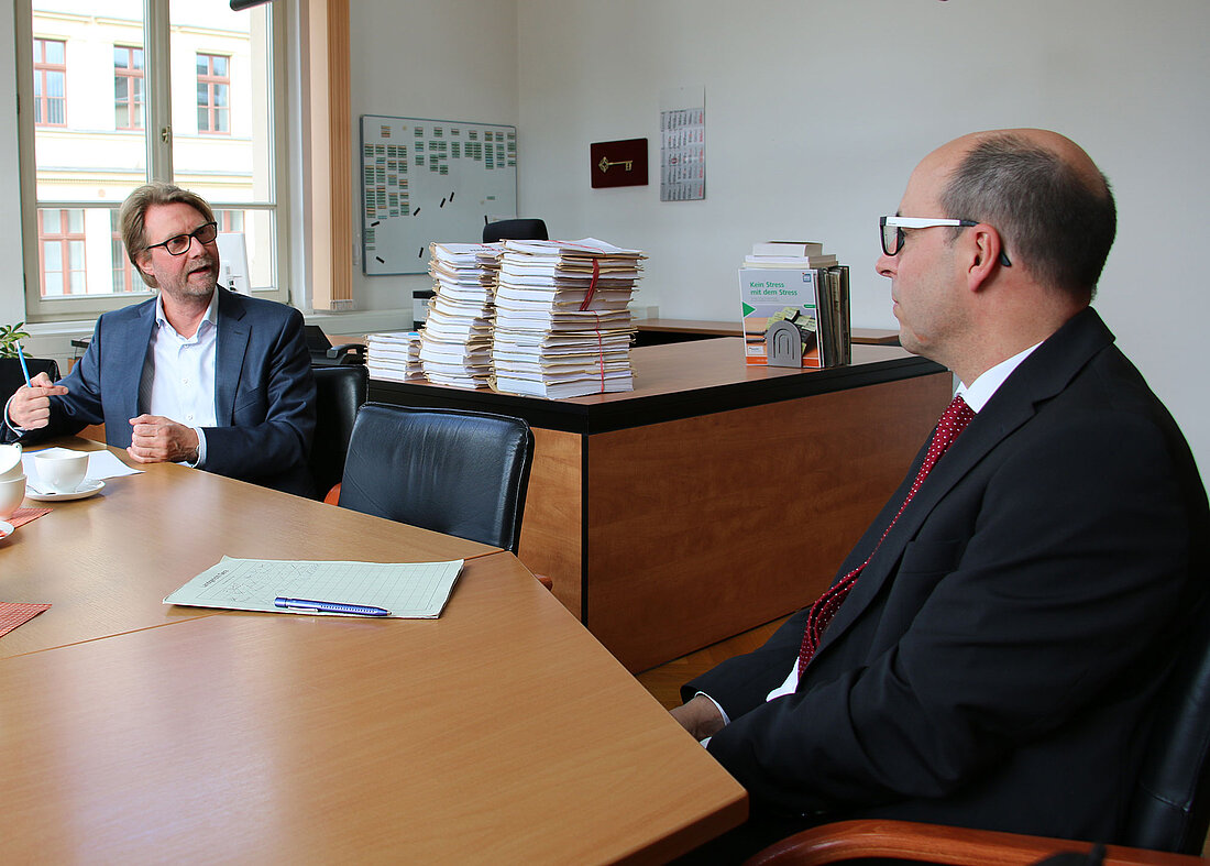 Justizminister Dirk Adams sitzt zusammen mit dem Vizepräsidenten des Landgerichts Gera, Dr. Götz Herrmann am Tisch und unterhält sich.