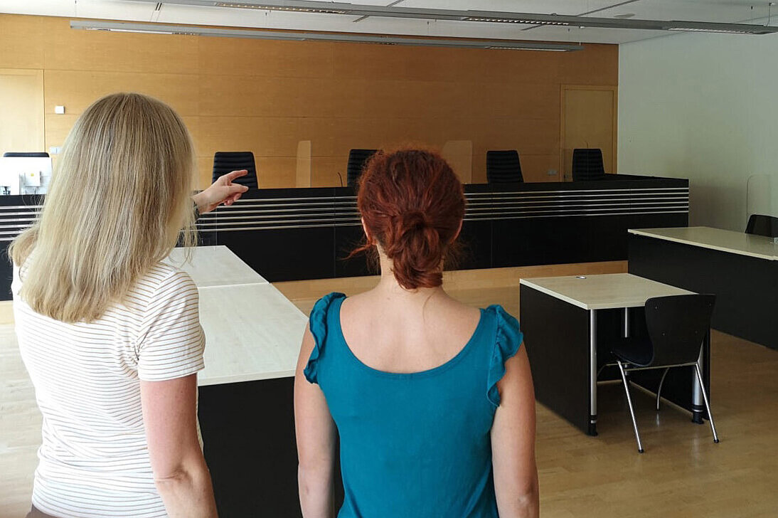 Eine psychosoziale Prozessbegleiterin zeigt einer Geschädigten den Verhandlungssaal..