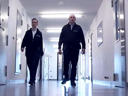 Zwei Justizvollzugsbeamte laufen über einen Gang im Hafthaus einer Justizvollzugsanstalt