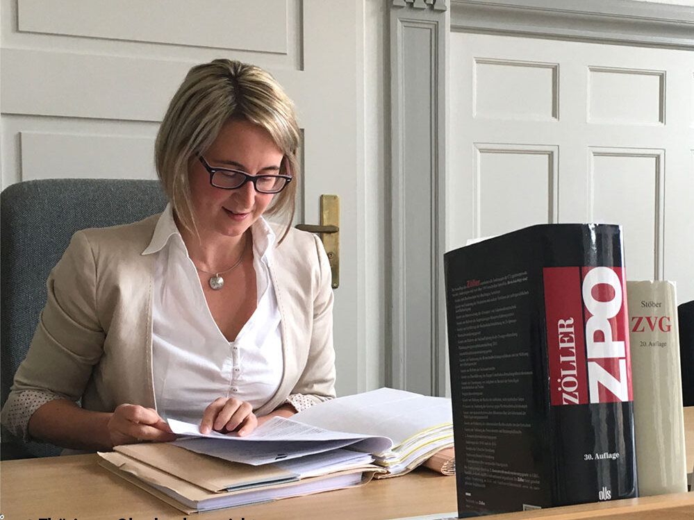 Rechtspflegerin am Schreibtisch sitzend während der Aktenbearbeitung mit sichtbaren 2 Gesetzbüchern