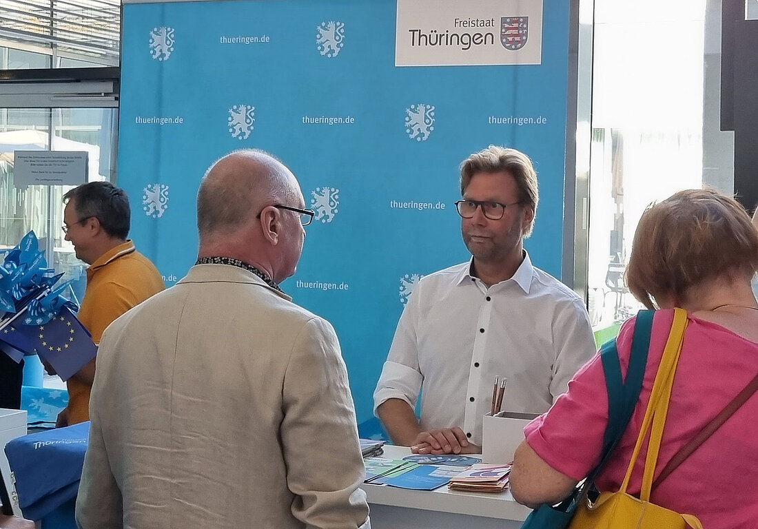 Minister Dirk Adams im Gespräch mit Bürgerinnen und Bürgern am Infostand der Thüringer Landesregierung beim Tag der offenen Tür im Thüringer Landtag.