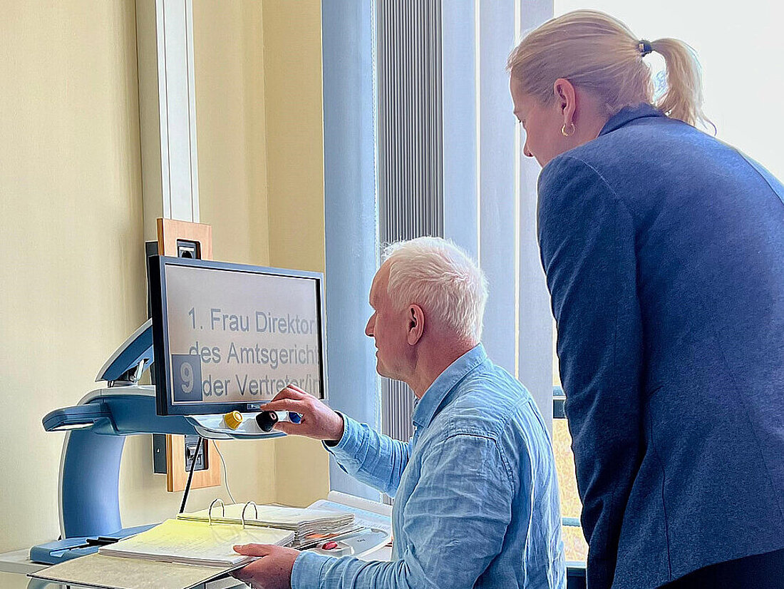 Justizministerin Beate Meißner lässt sich vom Vorsitzenden der Schwerbehindertenvertretung Dirk Fröb die Arbeit mit unterstützenden Technologien zeigen.