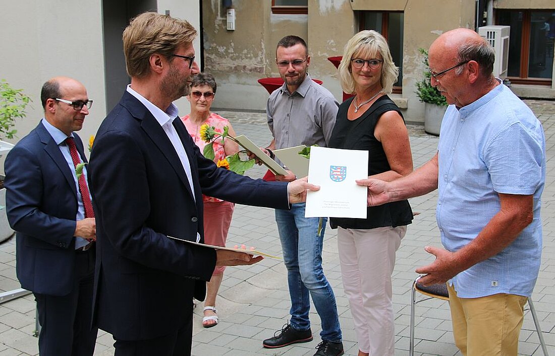 Justizminister Dirk Adamsk und der Vizepräsident des Landgerichts Gera, Dr. Götz Herrmann übergeben den Ehrenamtlichen die Urkunden und Präsente.