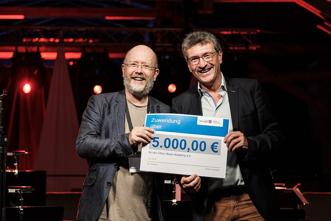 Minister Dieter Lauinger mit Andreas Schmitges vom Other Music Academy e. V. (OMA), Weimar, freudig einen Lottomitterlscheck über 5.000 EURO in den Händen haltend