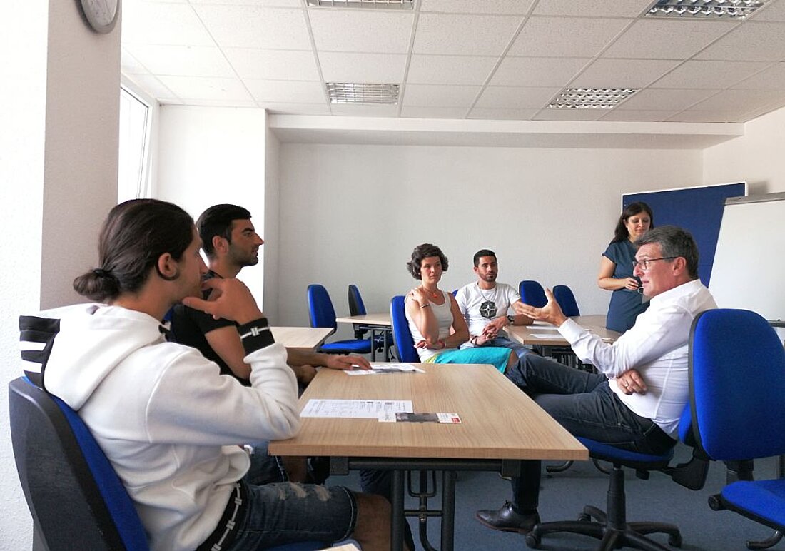 Minister Lauinger sitzend mit 2 männlichen Personen im Gespräch und 3 weitere anwesende Personen