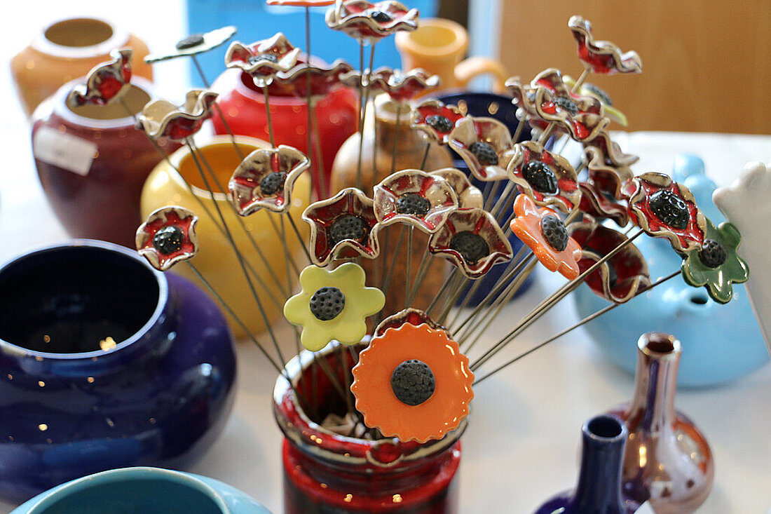 Bunte Blumen aus Ton in einer Vase und verschiedene Tongefäße daneben