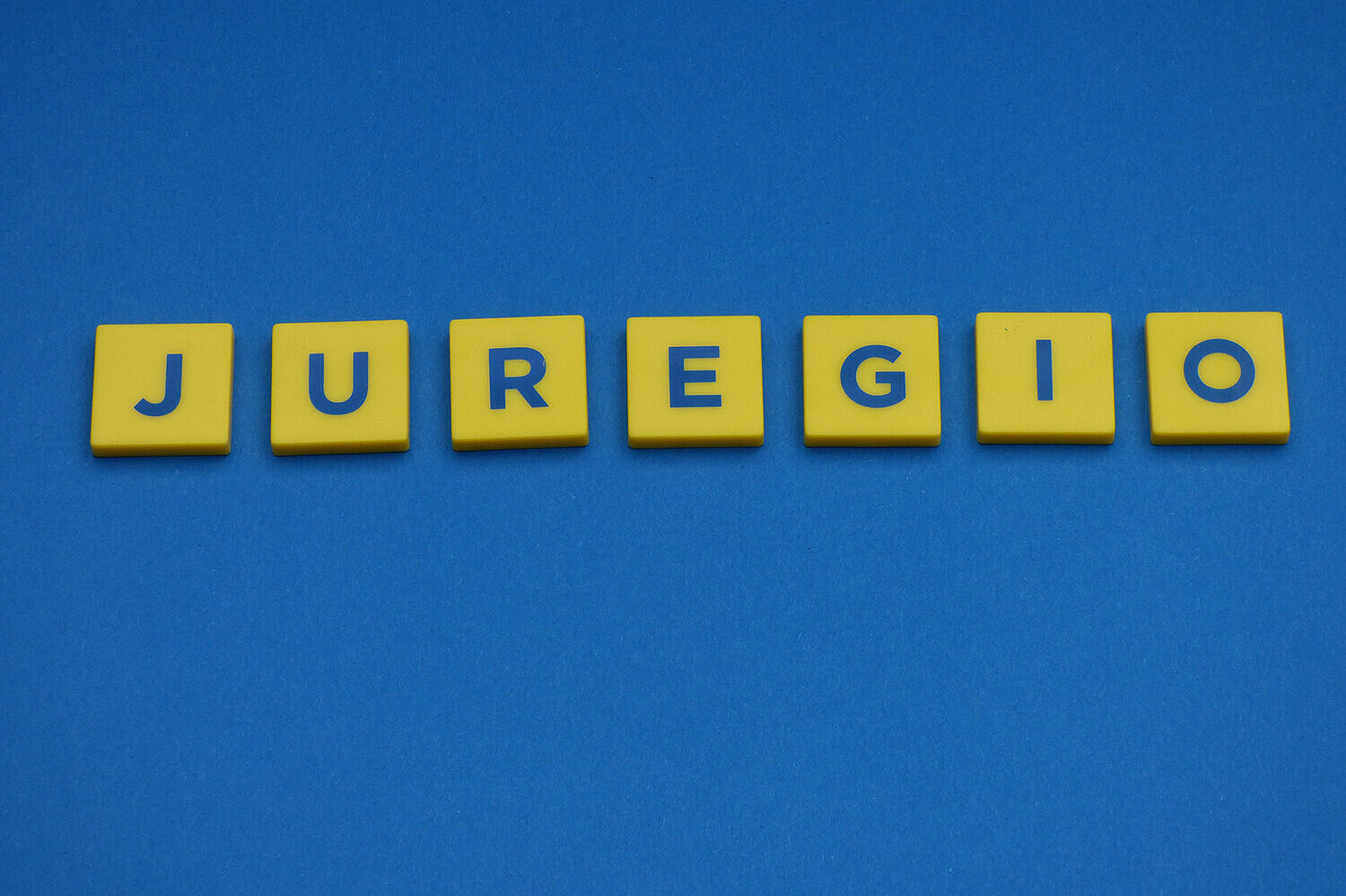 Schriftzug Juregio mit gelben Buchstabensteinen auf blauem Hintergrund gelegt