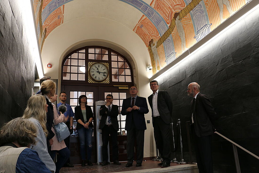 Minister Lauinger mit weiteren Personen im Kreis stehend und das gestaltete Portal des Gerichtes betrachtend