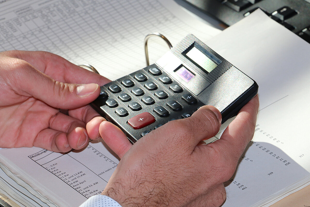 Hände mit einem Taschenrechner und einem Ordner mit Tabellen