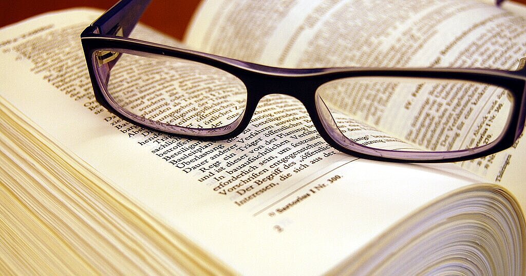 Aufgeschlagener Gesetzestext mit darauf liegender Sehhilfe
